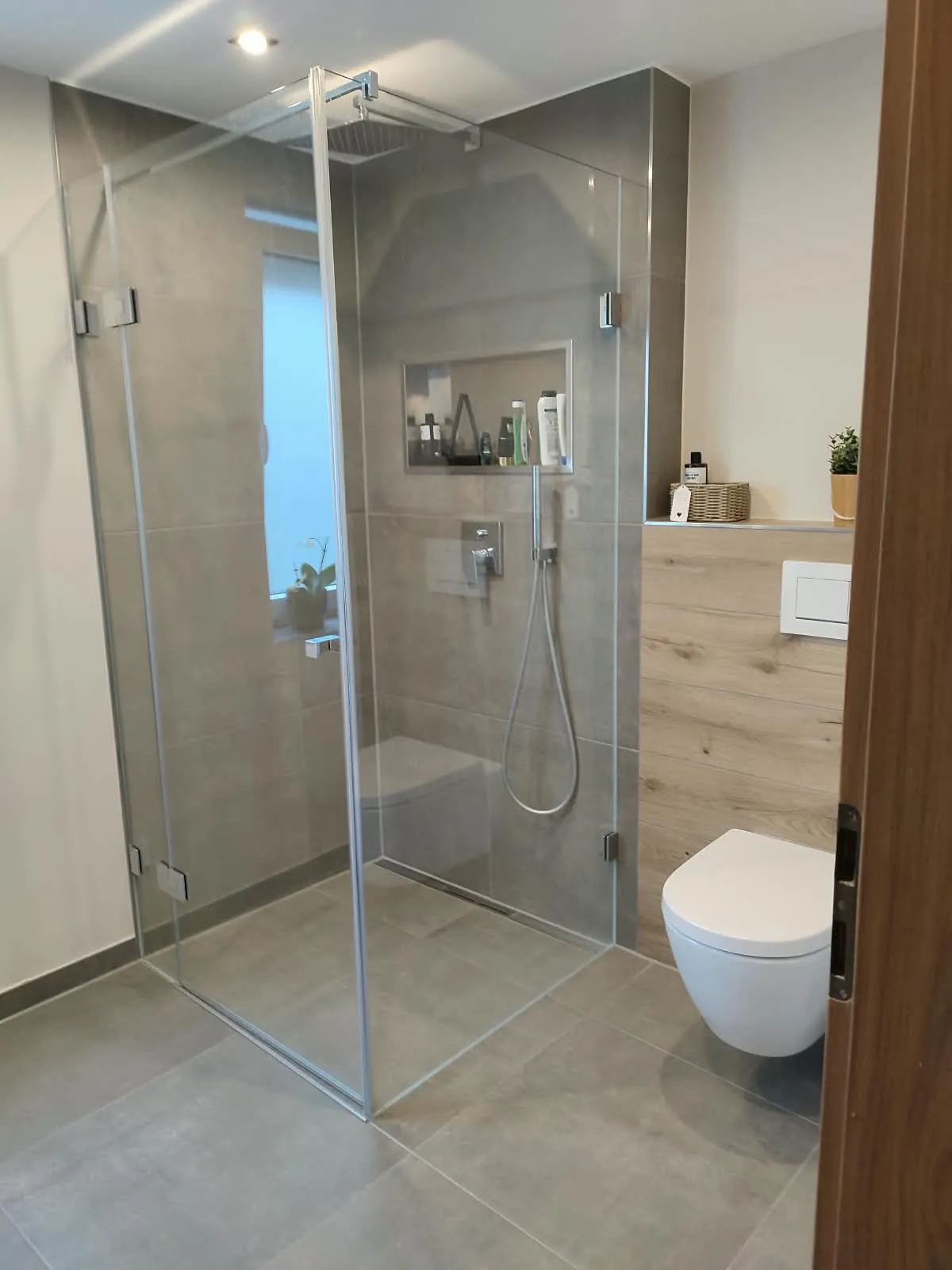 Dasselbe Bad nach der Sanierung — bodengleiche Glasdusche und WC an der Holzoptik-Vorwand