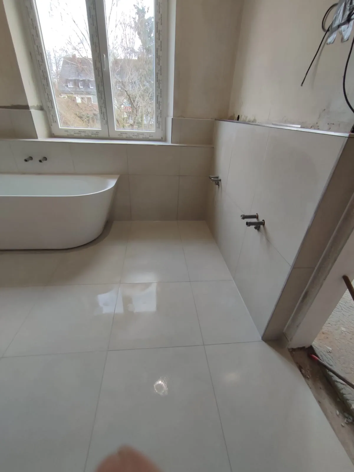 Bad nach der Renovierung — freistehende Wanne, glänzende Großformatfliesen