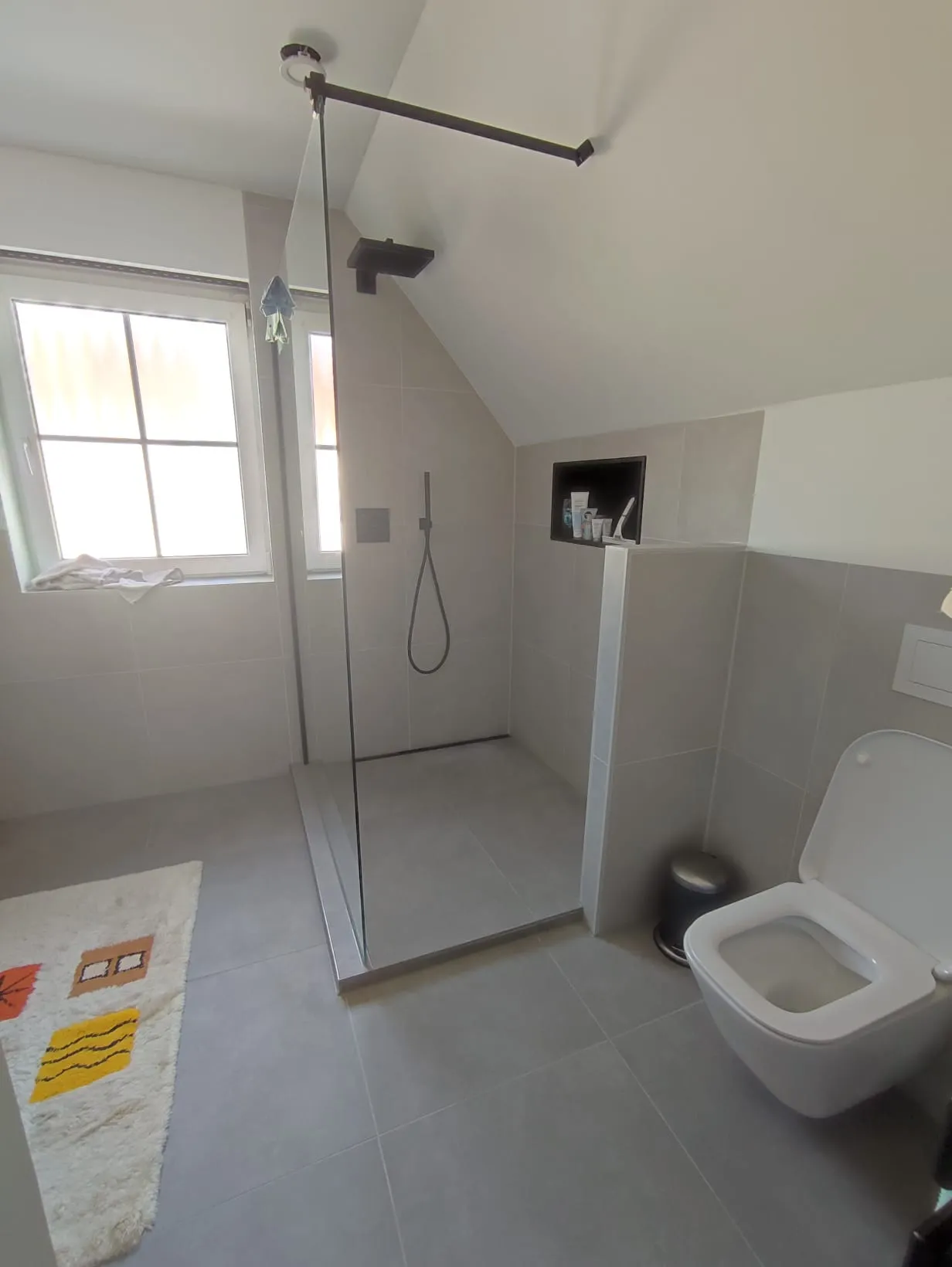 Dieselbe Ecke fertig — bodengleiche Dusche mit Glasabtrennung und WC an der Vorwand